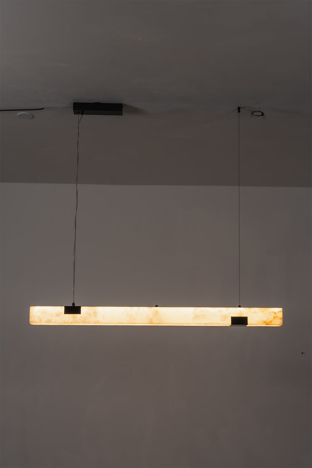 Liora Linear Alabaster Pendant Light | Natural Alabaster and Black Metal | Minimalist full view of the illuminated linear pendant light glowing in a dimly lit environment | Samu Lamp