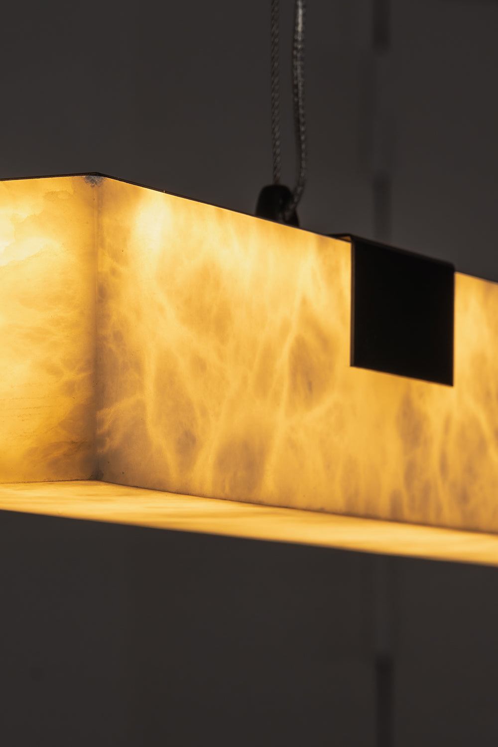Liora Linear Alabaster Pendant Light | Natural Alabaster and Black Metal | Detailed macro shot focusing on the warm light filtering through the marbled stone texture | Samu Lamp