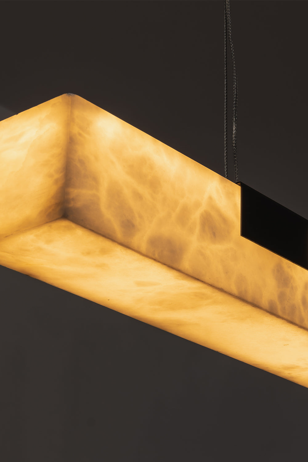 Liora Linear Alabaster Pendant Light | Natural Alabaster and Black Metal | Close-up macro view highlighting the corner of the glowing alabaster stone and a black bracket | Samu Lamp