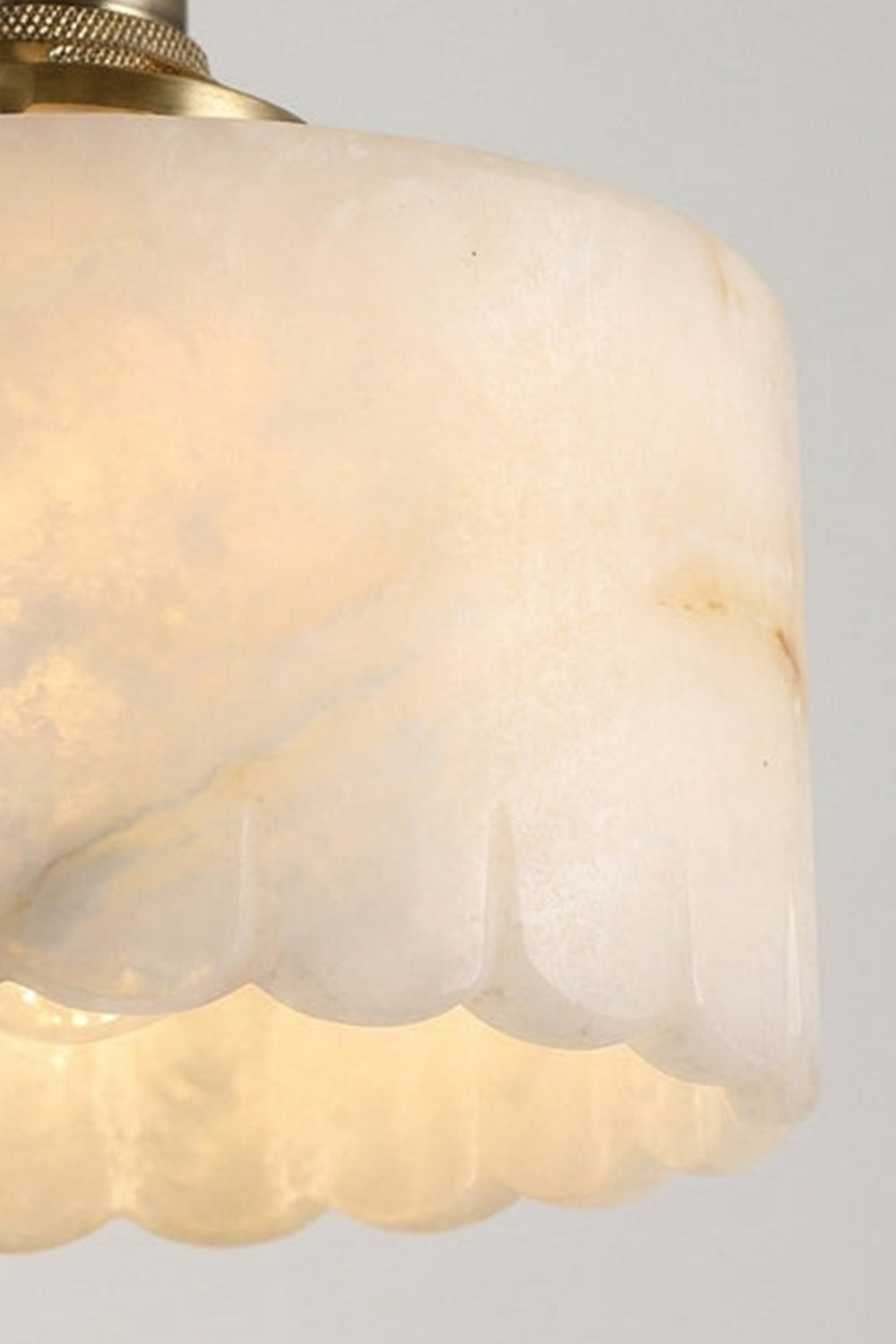 Liora Scalloped Alabaster Wall Sconce | Natural Alabaster and Brushed Brass | Macro close-up shot focusing on the intricate wavy scalloped bottom edge of the lit translucent stone shade | Samu Lamp