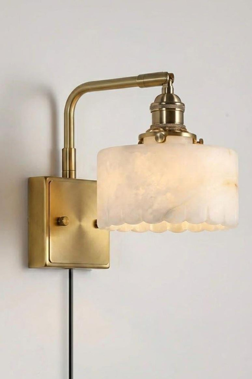 Liora Scalloped Alabaster Wall Sconce | Natural Alabaster and Brushed Brass | Standard studio single product view hanging fully lit with a plug-in cord against a light grey background | Samu Lamp