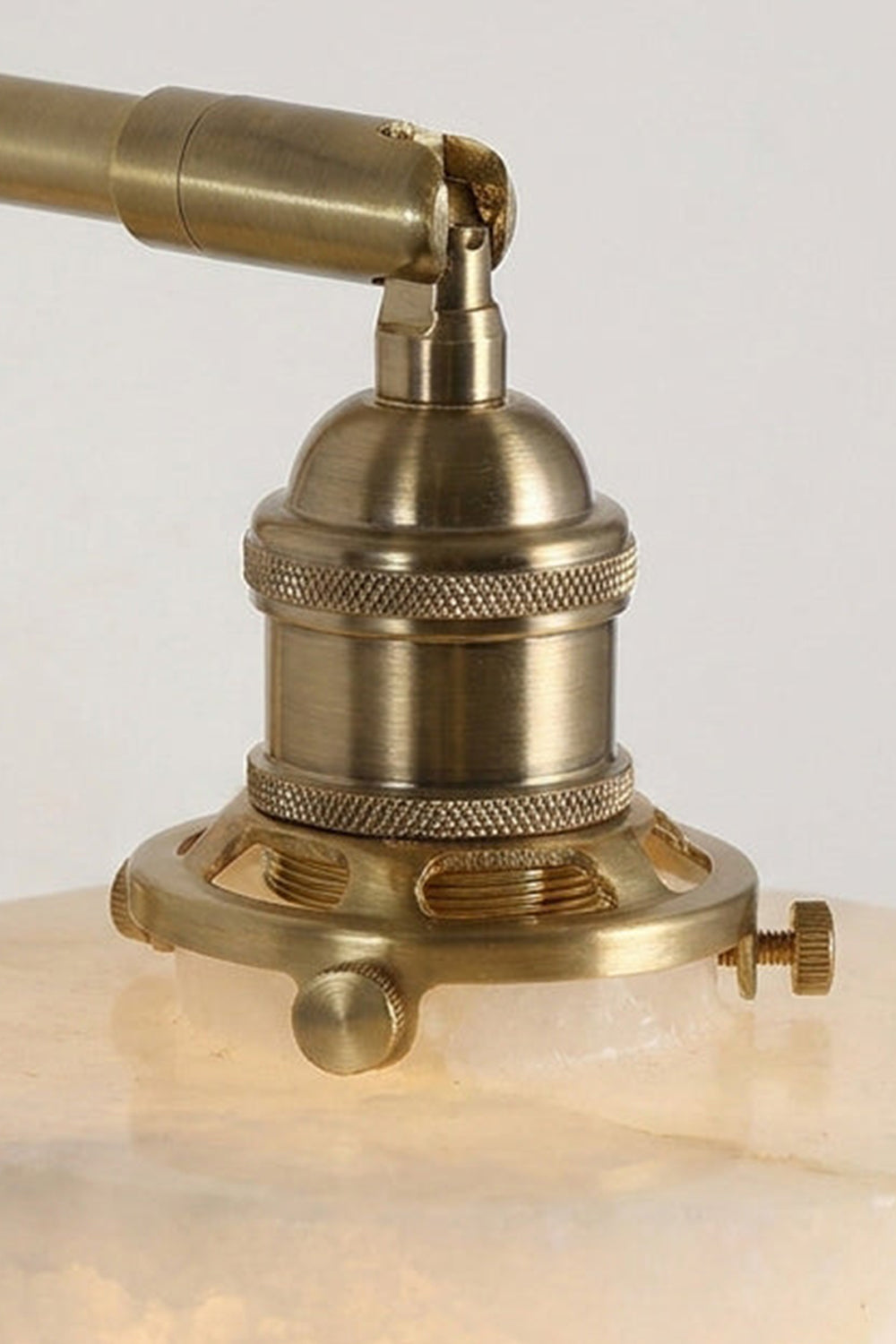 Liora Scalloped Alabaster Wall Sconce | Natural Alabaster and Brushed Brass | Extreme close-up preview of the polished brass hardware socket and top screw connections on the stone shade | Samu Lamp