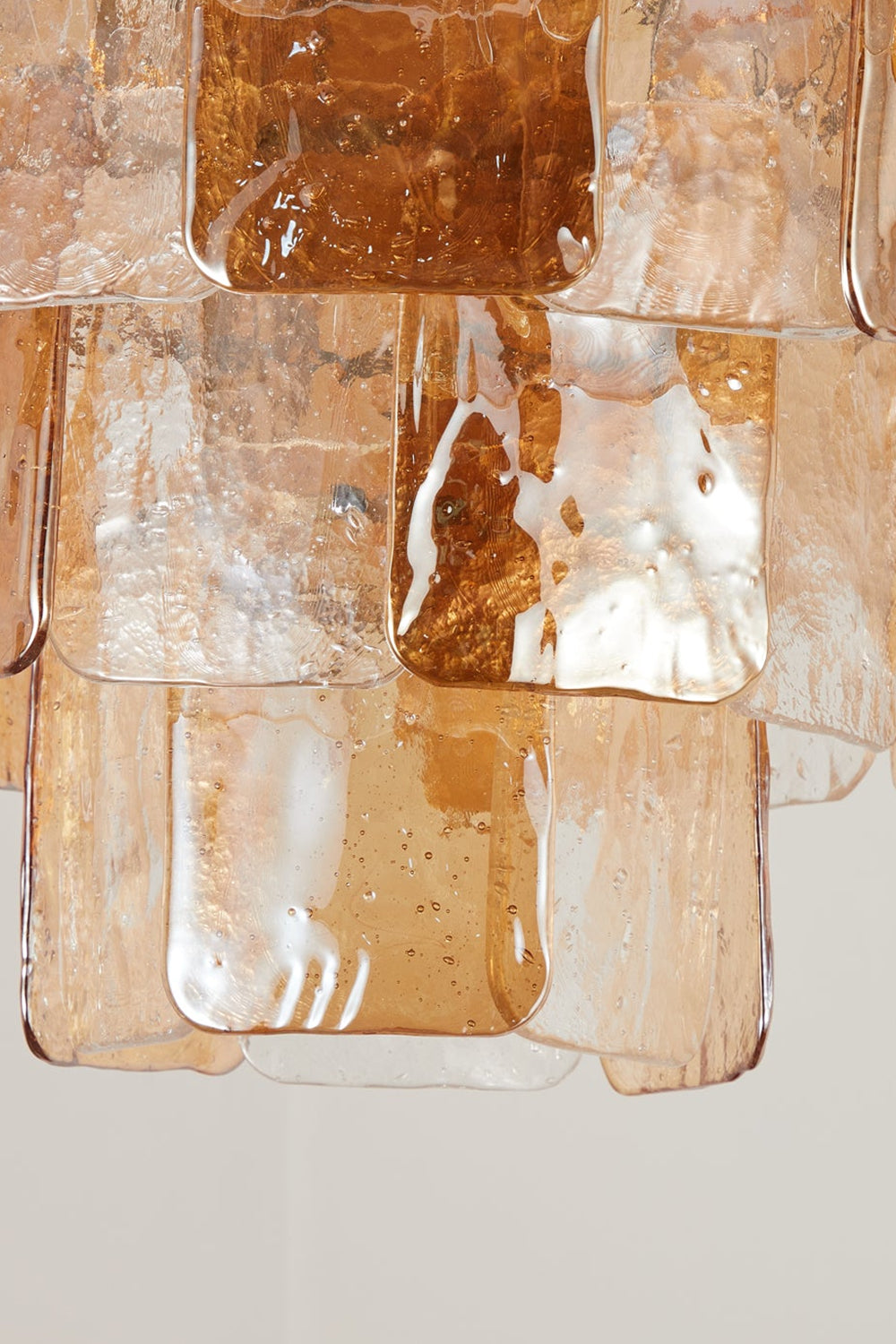Lucia Tiered Amber Glass Chandelier | Glass, Metal | Close-up focus on the illuminated textured amber glass panels highlighting the crinkled ice-like surface and warm light transmission | Detail shot | Samu Lamp