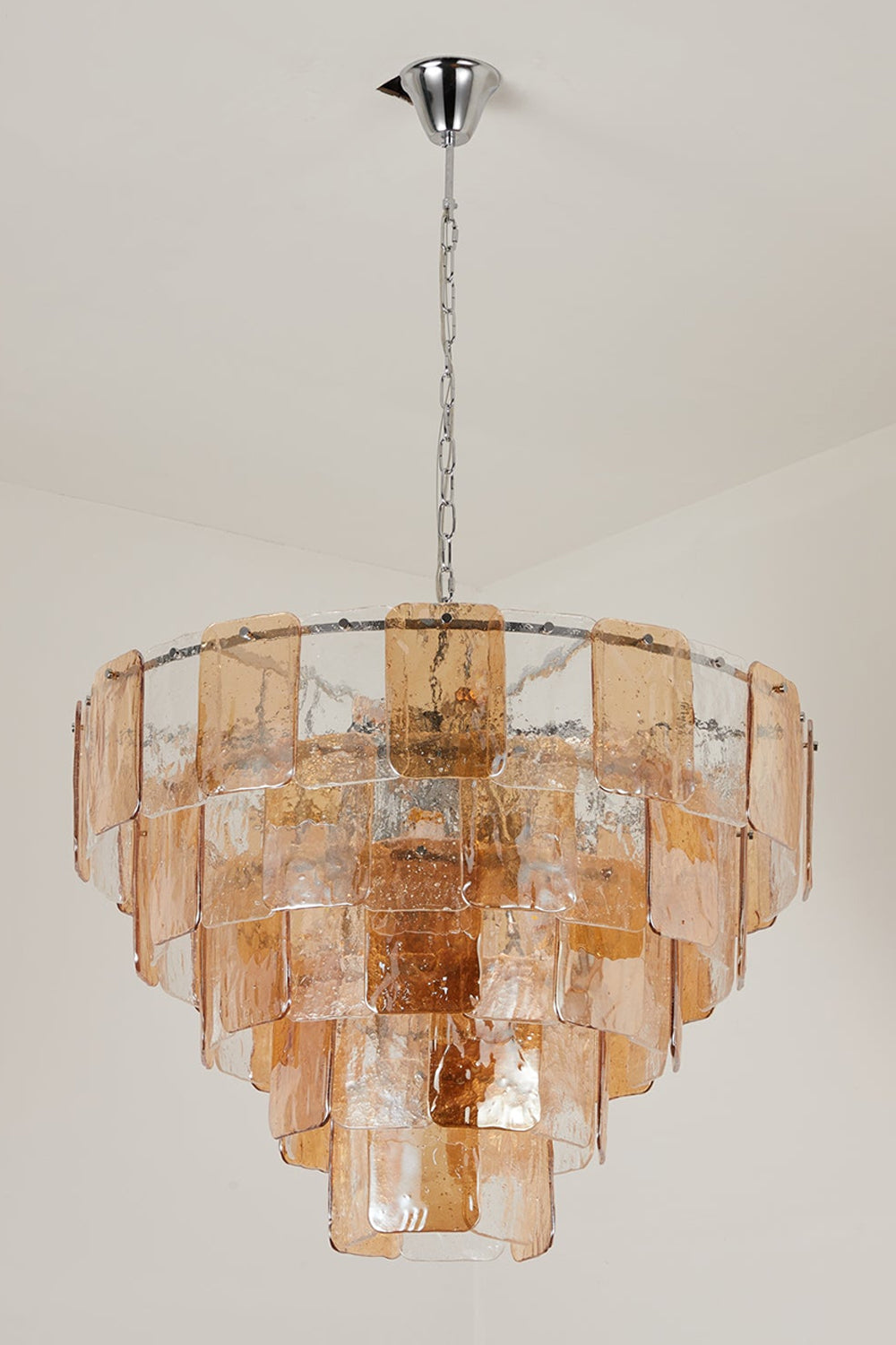 Lucia Tiered Amber Glass Chandelier | Glass, Metal | Studio front view of the fully illuminated multi-tier amber glass chandelier casting a warm golden light against a grey backdrop | Samu Lamp