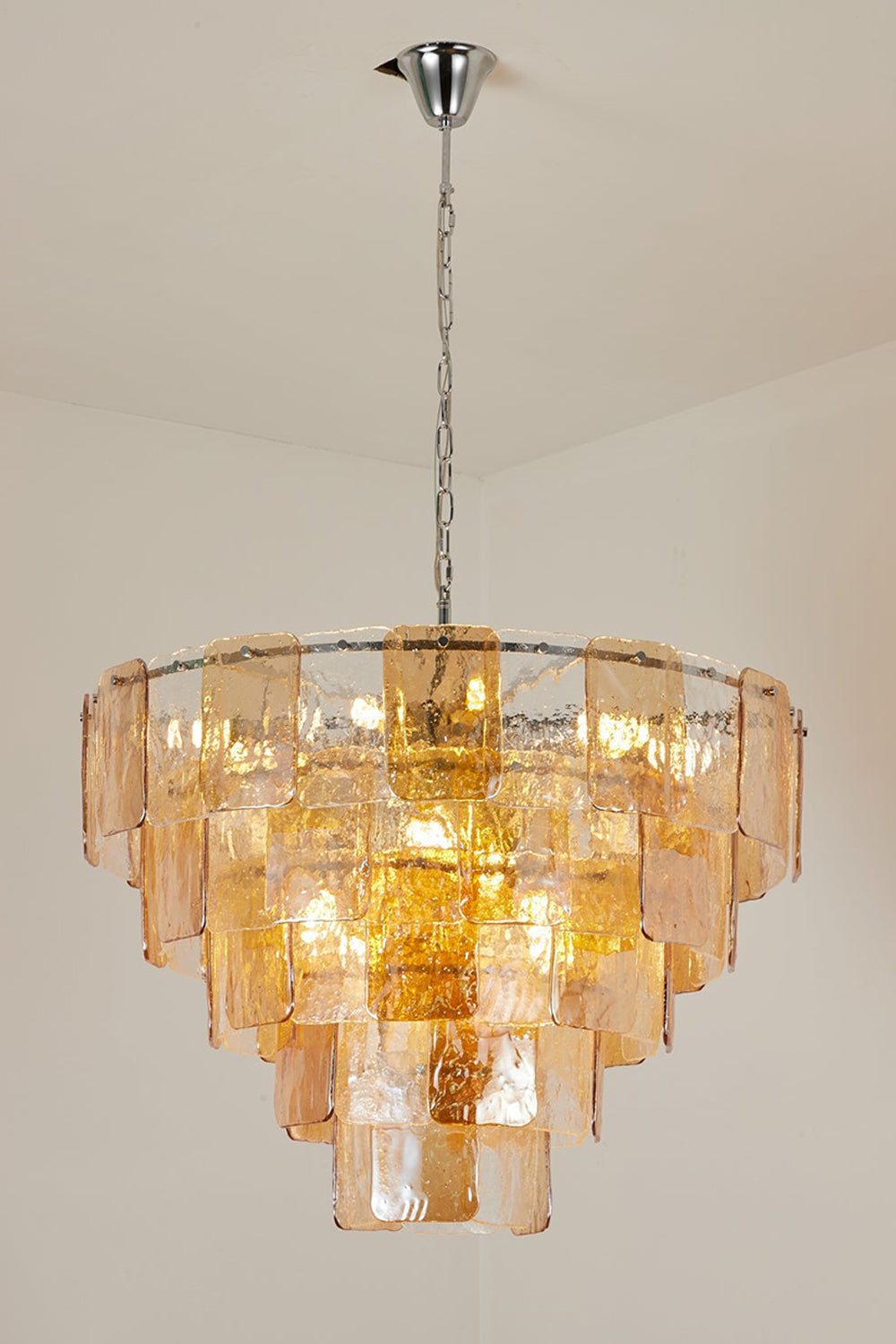 Lucia Tiered Amber Glass Chandelier | Glass, Metal | Alternative full studio shot of the illuminated tiered glass light fixture hanging elegantly against a grey studio backdrop | Samu Lamp