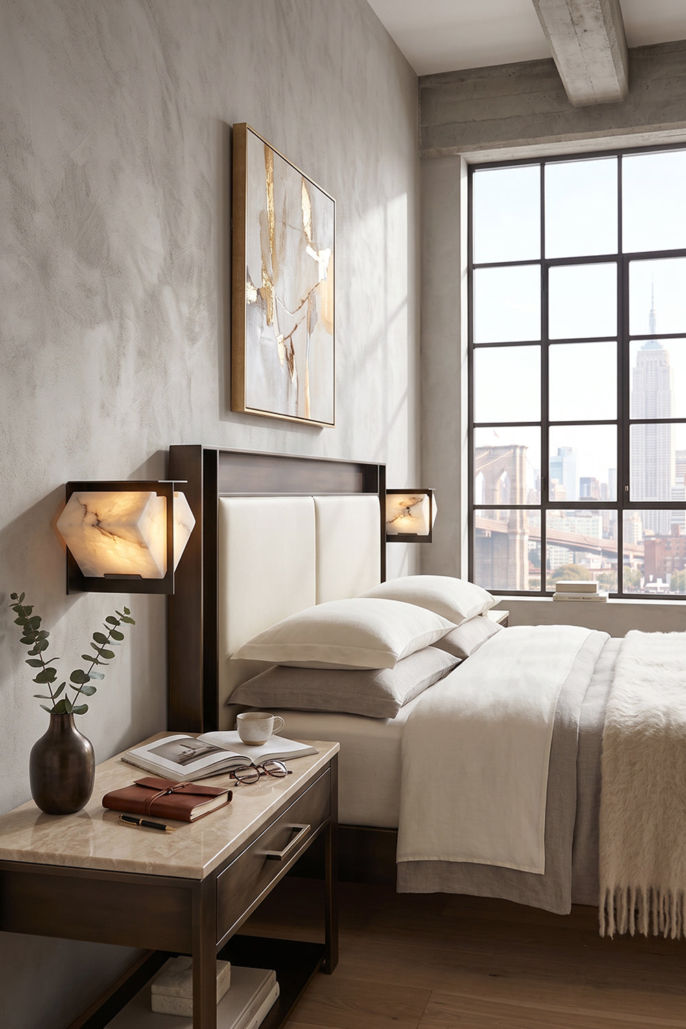 Lysandra Alabaster Folded Halo Wall Lamp | Bedroom Lighting | Mounted as an elegant bedside lamp casting a warm golden glow next to a cream platform bed in an industrial loft bedroom | Samu Lamp