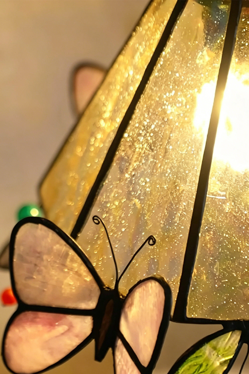 Mariposa Canopy Stained Glass Pendant Lamp | Glass, Metal | Close-up view of the illuminated amber textured glass and a delicate pink butterfly element from the side | Detail shot | Samu Lamp