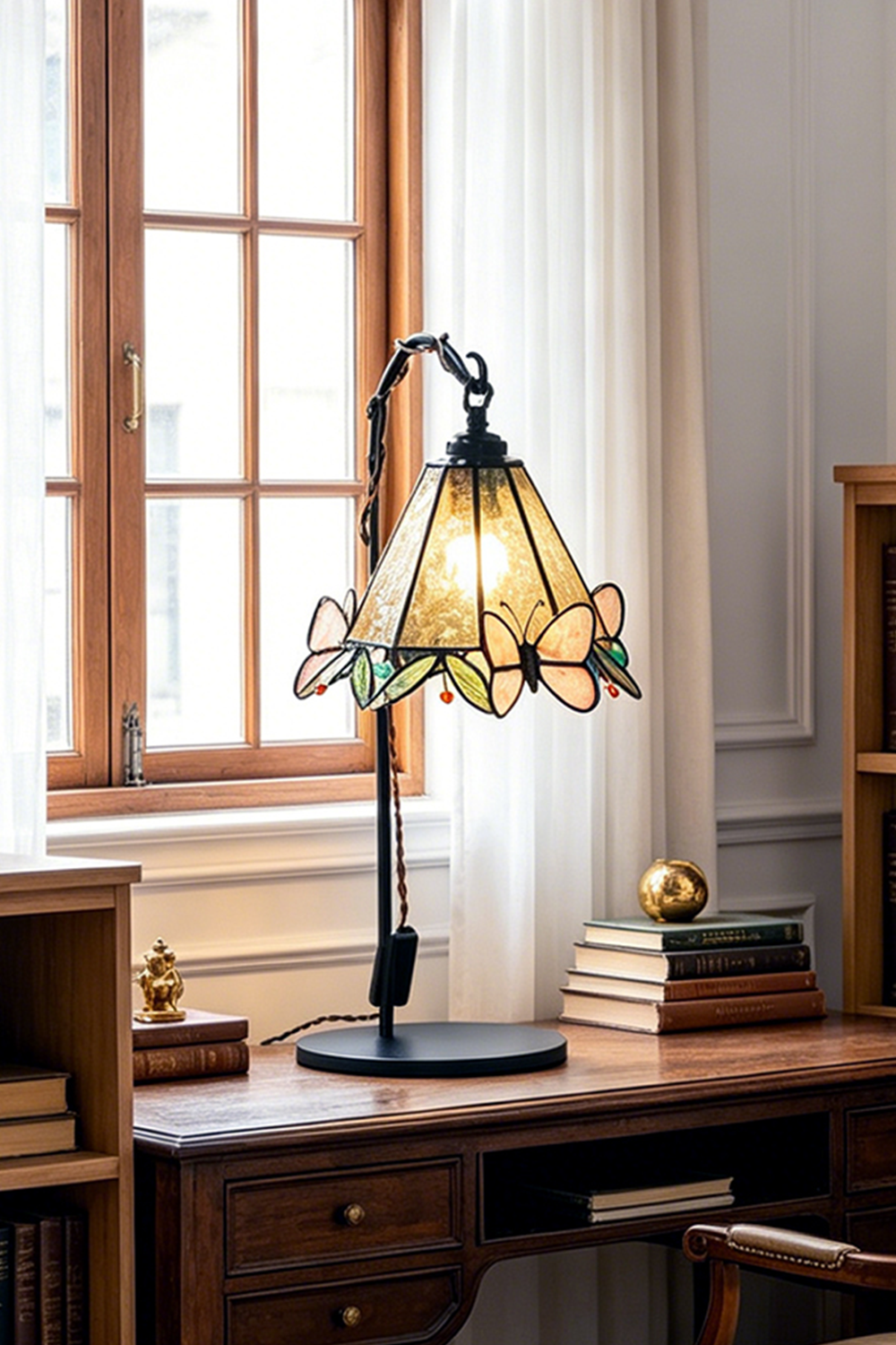 Mariposa Stained Glass Table Lamp | Glass, Metal | Placed on a vintage dark wood desk in front of a bright arched window in a cozy study | Samu Lamp