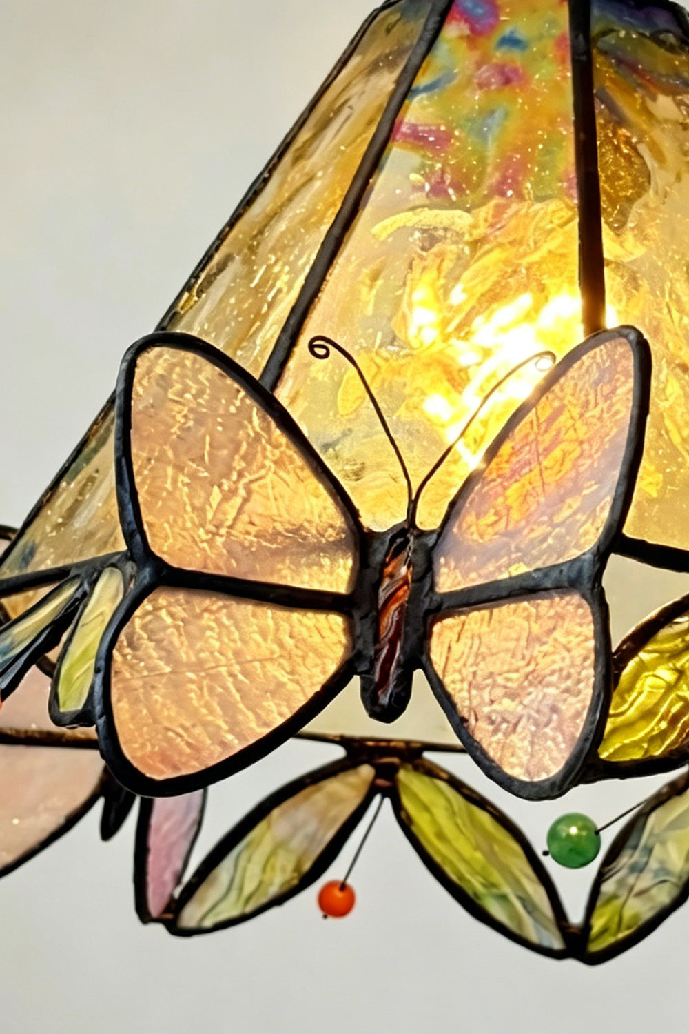 Mariposa Stained Glass Table Lamp | Glass, Metal | Close-up of the illuminated shade showcasing a vibrant yellow-orange butterfly wing pattern and glass gems | Detail shot | Samu Lamp