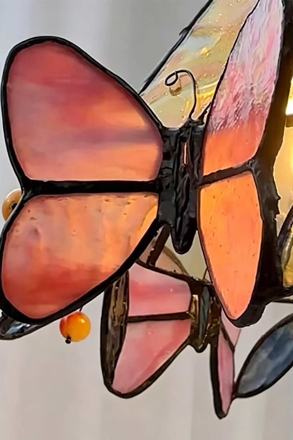 Mariposa Stained Glass Table Lamp | Glass, Metal | Macro focus on a translucent pink and orange stained glass butterfly element along the shade's edge | Detail shot | Samu Lamp