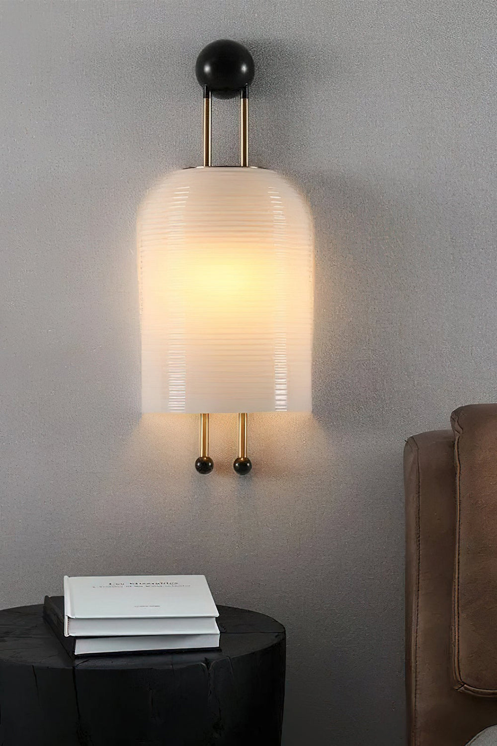 Marlow Linear Ribbed Glass Wall Lamp | Glass, Metal | Close-up shot of the lit ribbed sconce on a grey textured wall casting a warm glow over a black nightstand with a book | Samu Lamp