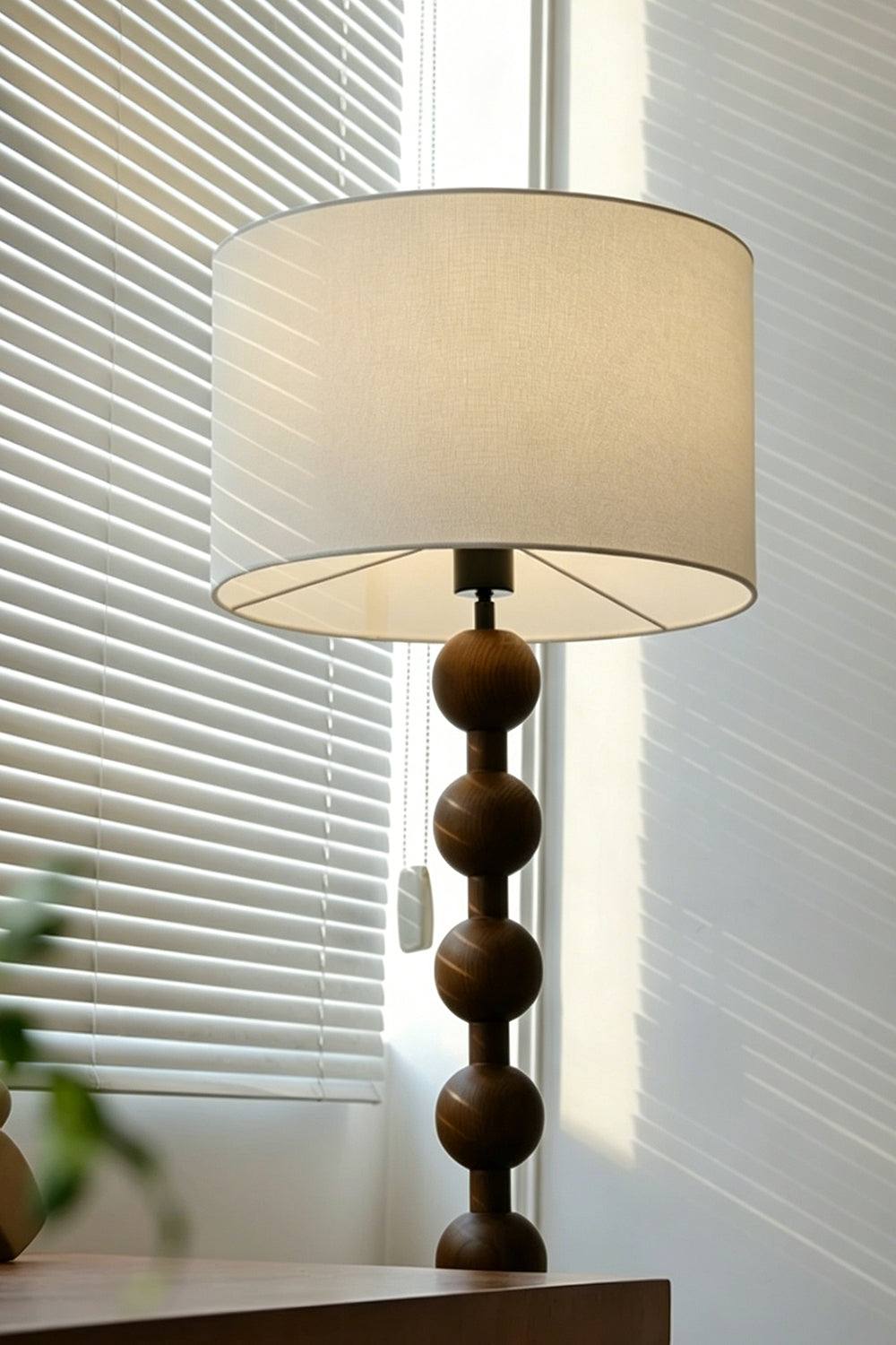 Marlow Stacked Wood Floor Lamp | Wood, Fabric | Upper section of the bobbin floor lamp near a window with slatted blinds, highlighting the interplay of natural light and shadow on the shade | Detail shot | Samu Lamp