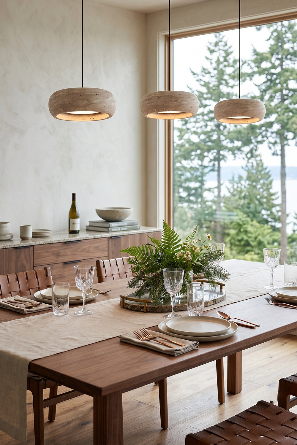 Maro Travertine Donut Pendant Light | Travertine, Metal | Three linear stone pendant fixtures hung above a contemporary wood dining table in a sunlit open-concept home interior | Samu Lamp
