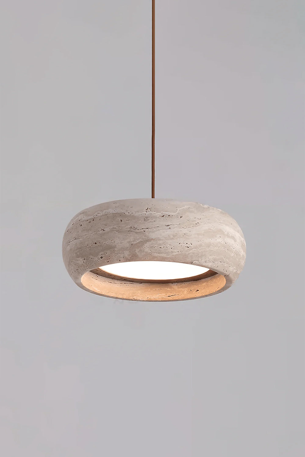 Maro Travertine Donut Pendant Light | Travertine, Metal | Studio product view of the fully illuminated travertine donut pendant light casting a cozy golden halo on a grey background | Samu Lamp