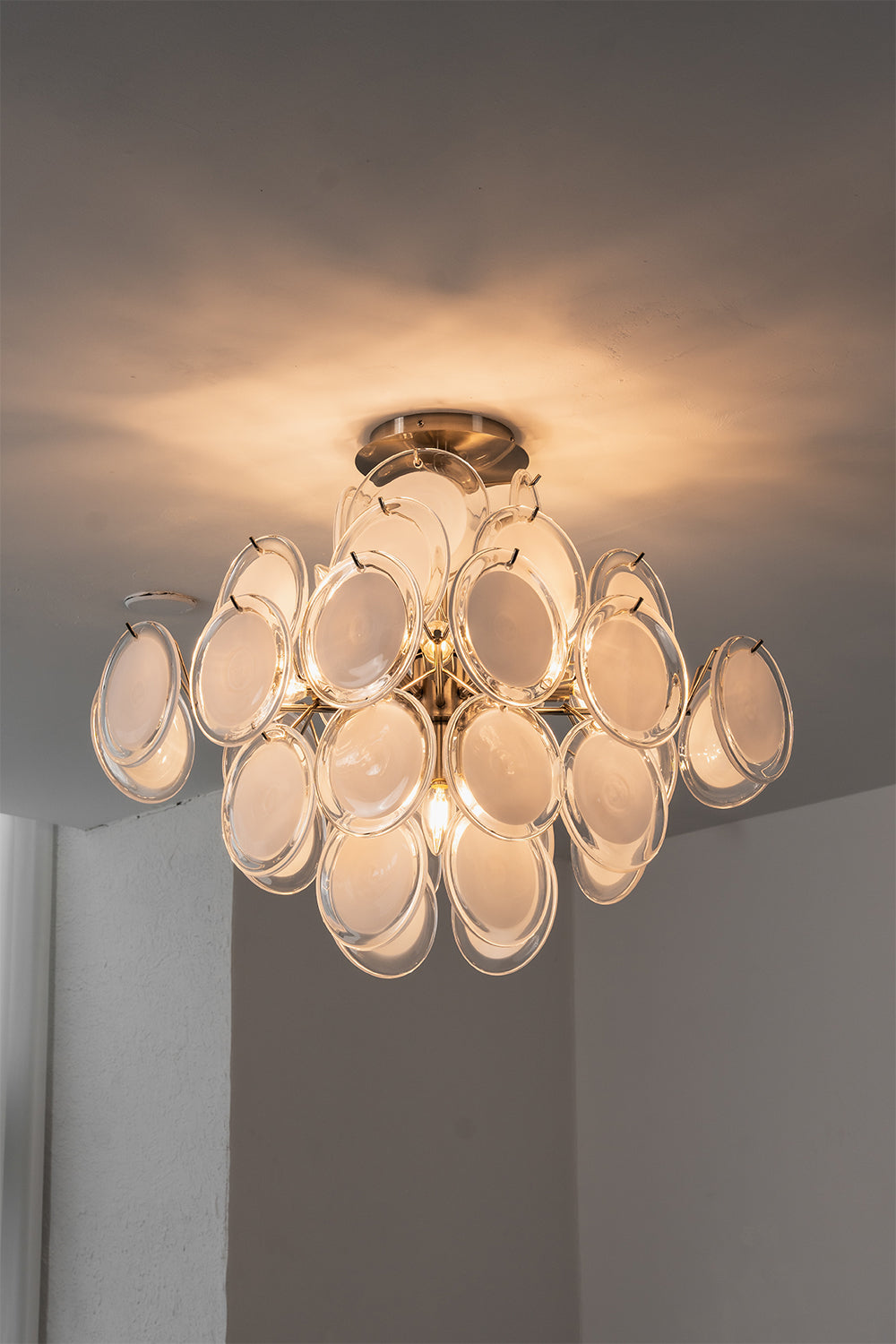 Mirella Circular Glass Pane Ceiling Light | Studio Lit View | Fully lit studio presentation of the circular glass pane fixture casting a warm golden light halo on a grey ceiling backdrop | Samu Lamp