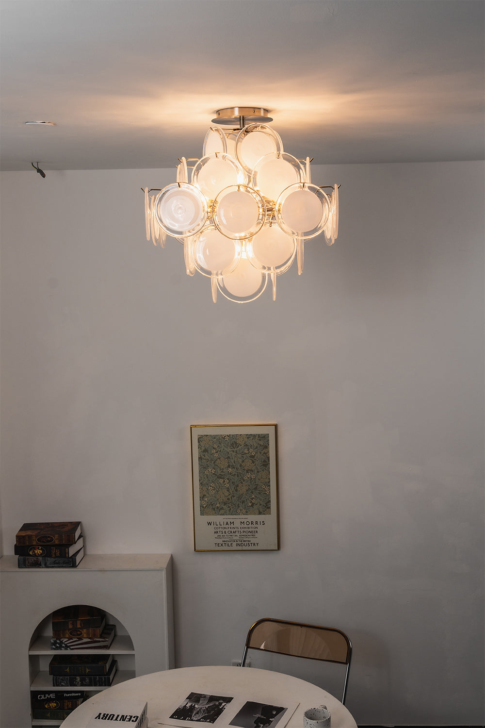 Mirella Circular Glass Pane Ceiling Light | Room Staged View | Studio lit display of the modern multi-glass disc ceiling light hanging against a plain wall above a minimalist table | Samu Lamp