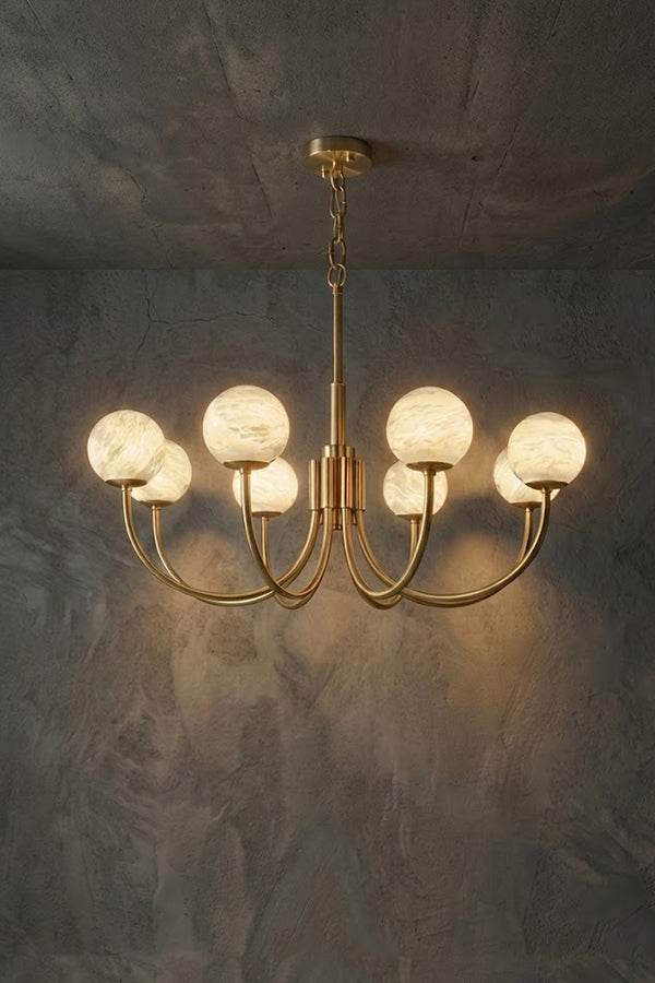 Lit modern brass globe chandelier | Alabaster, Brass | Front view against a textured grey wall | Samu Lamp                 