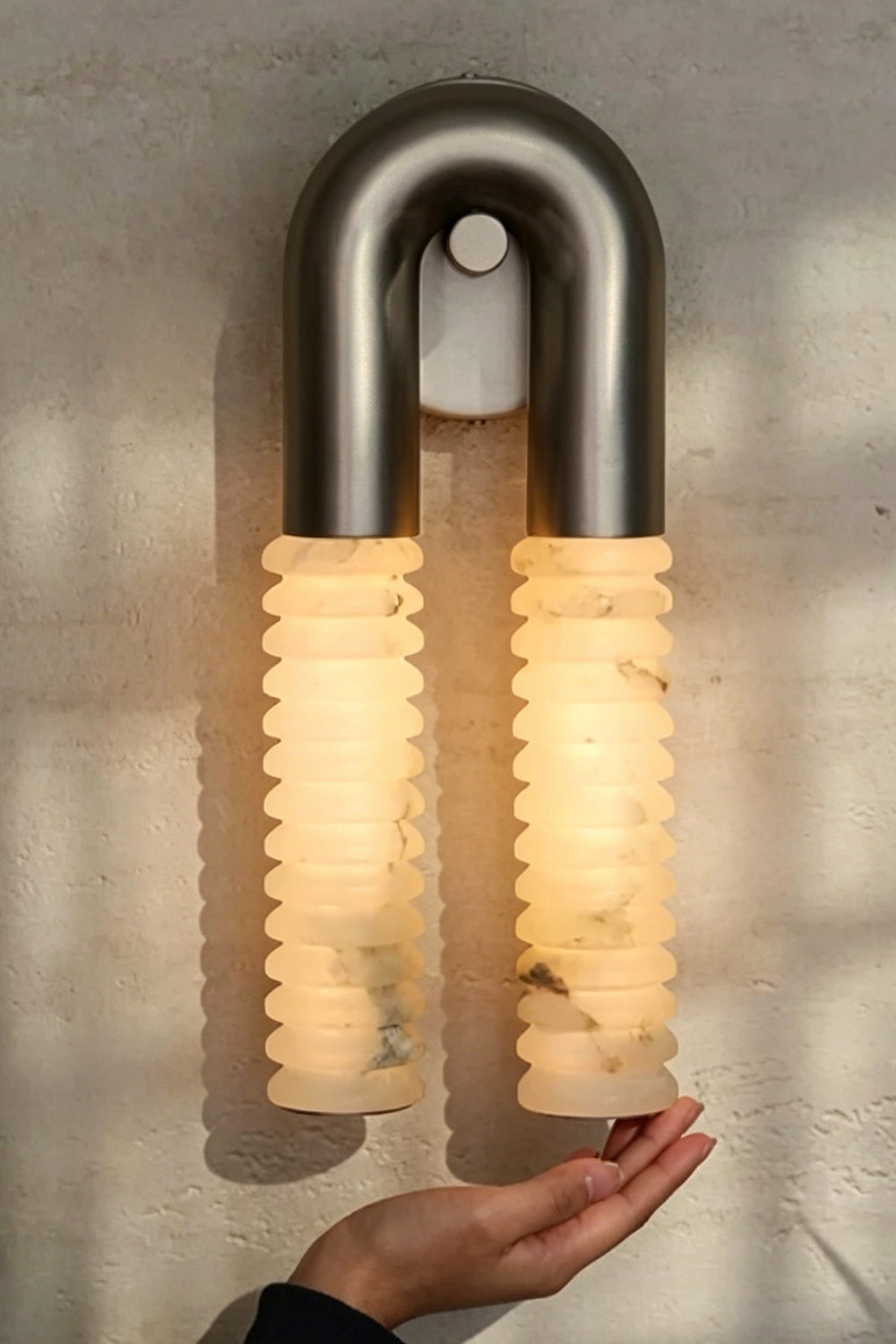 Monolith Arc Alabaster Wall Lamp | Alabaster, Metal | Fully lit lamp showing the warm translucency and scale next to a person's hand | Detail shot | Samu Lamp