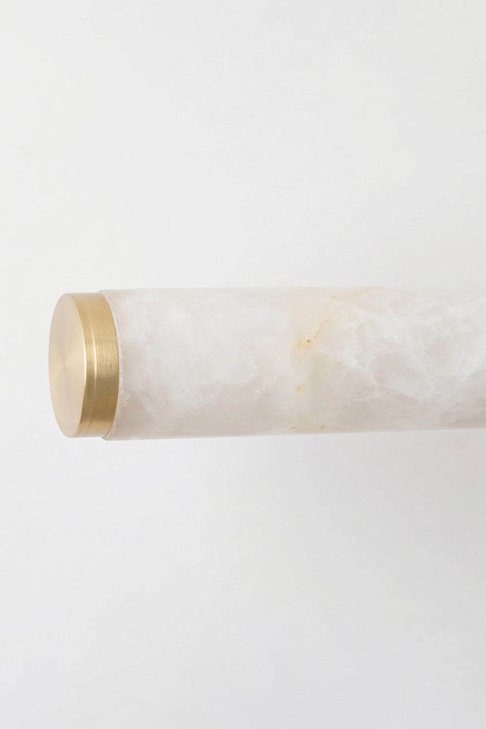 Nerida Linear Alabaster Wall Sconce | Alabaster, Brass | Close-up view focusing on the clean unlit end section of the natural white stone cylinder finished with a brushed gold brass end-cap | Detail shot | Samu Lamp