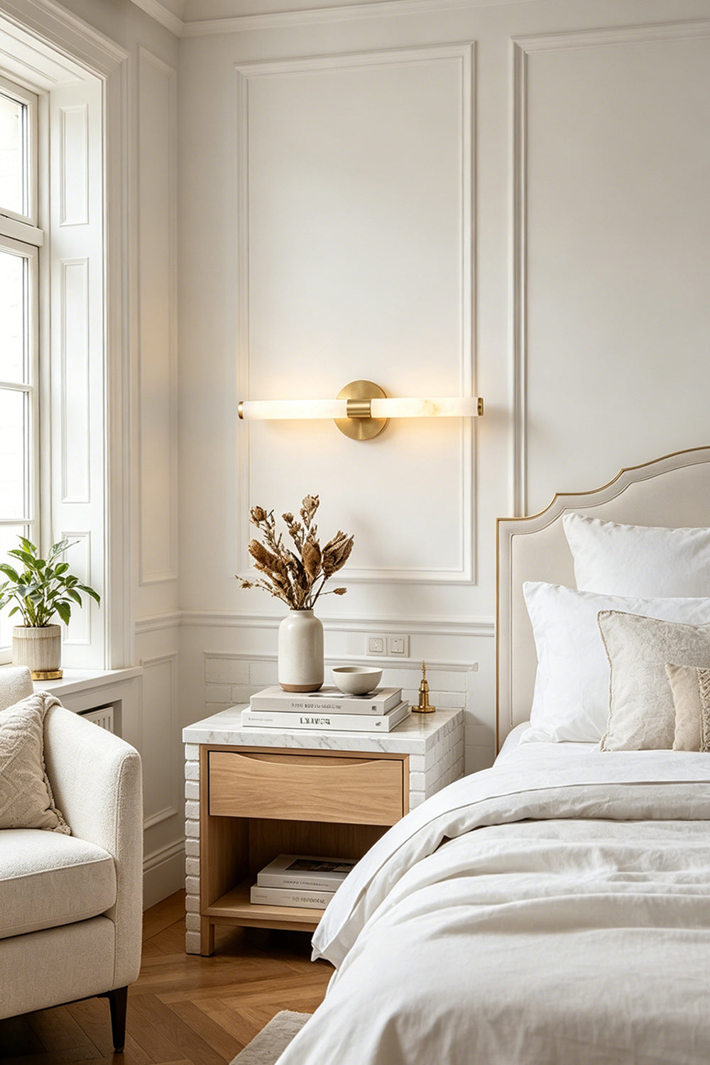 Nerida Linear Alabaster Wall Sconce | Alabaster, Brass | Mounted horizontally as an elegant bedtime light casting a warm golden glow above a wooden nightstand in a classical white bedroom | Samu Lamp