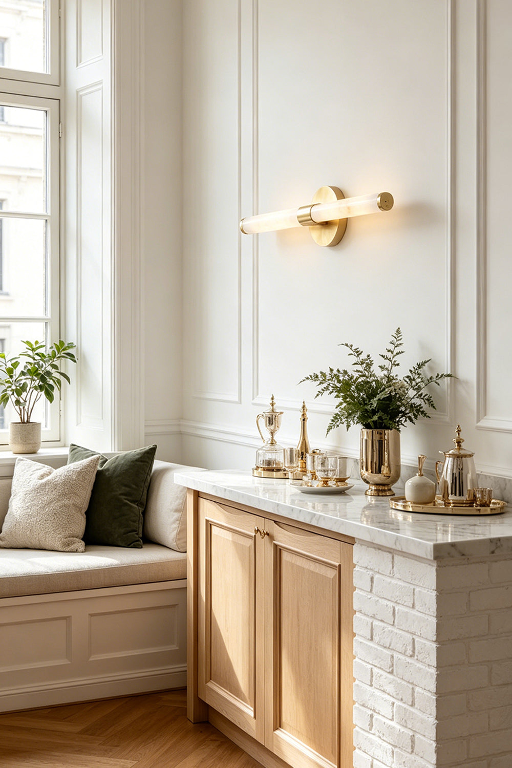 Nerida Linear Alabaster Wall Sconce | Alabaster, Brass | Positioned elegantly on a white paneled wall above a classic wooden sideboard cabinet with a marble top in a sunlit hallway lounge | Samu Lamp
