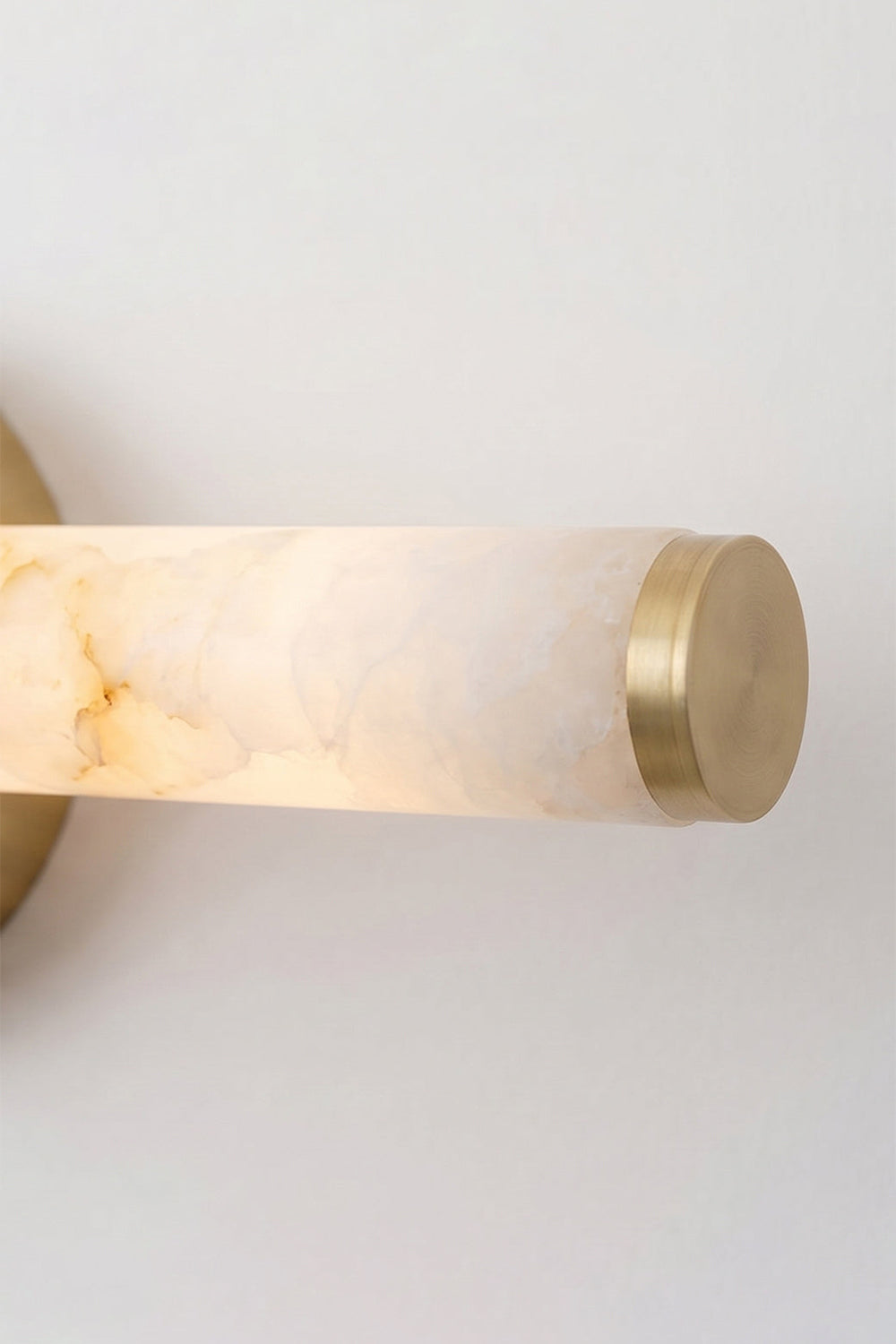 Nerida Linear Alabaster Wall Sconce | Alabaster, Brass | Detailed shot of the illuminated end of the alabaster tube showcasing a translucent soft warm glow and the matching gold brass cap | Detail shot | Samu Lamp