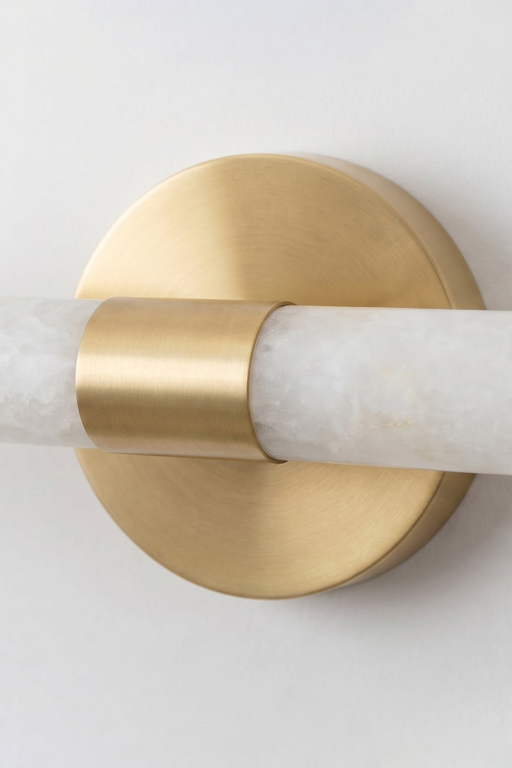 Nerida Linear Alabaster Wall Sconce | Alabaster, Brass | Detailed close-up shot focusing on the central circular brushed gold brass wall mounting plate and ring clamp holding the alabaster bar | Detail shot | Samu Lamp