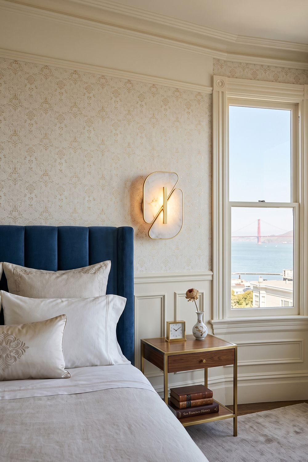 Nerine Overlapping Alabaster Wall Lamp illuminating a stylish bedroom with a view of San Francisco Bay.