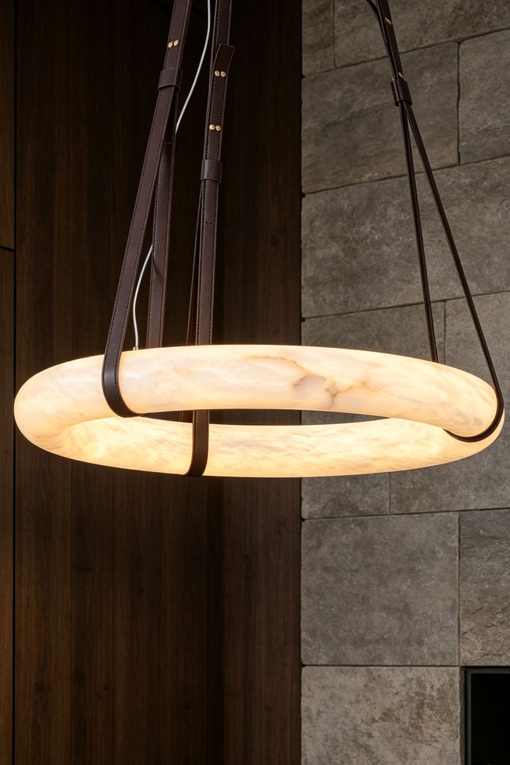 Nerissa Alabaster Ring Leather Pendant Light | Natural Alabaster, Leather and Brass | Close view of the 3-strap ring pendant hanging near a dark wood wall | Samu Lamp