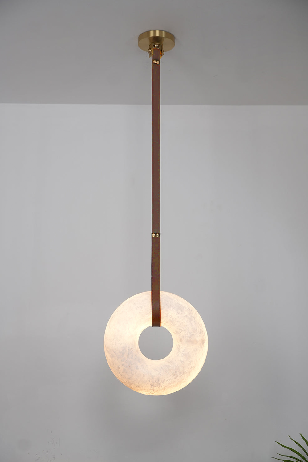 Nerissa Alabaster Ring Leather Pendant Light | Natural Alabaster, Leather and Brass | Single-strap disc variant full view hanging on a plain backdrop | Samu Lamp