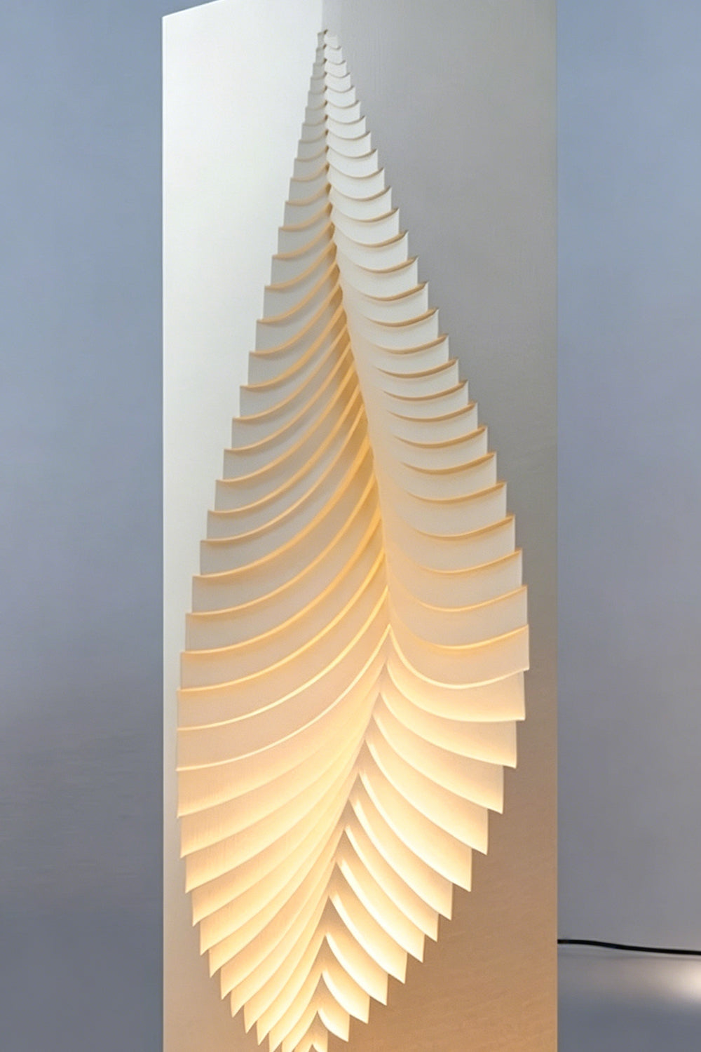 Nori Sculptural Leaf Floor Lamp | Fabric, Wood | Studio mockup shot of the tall column lamp glowing softly against a clean light grey backdrop | Samu Lamp
