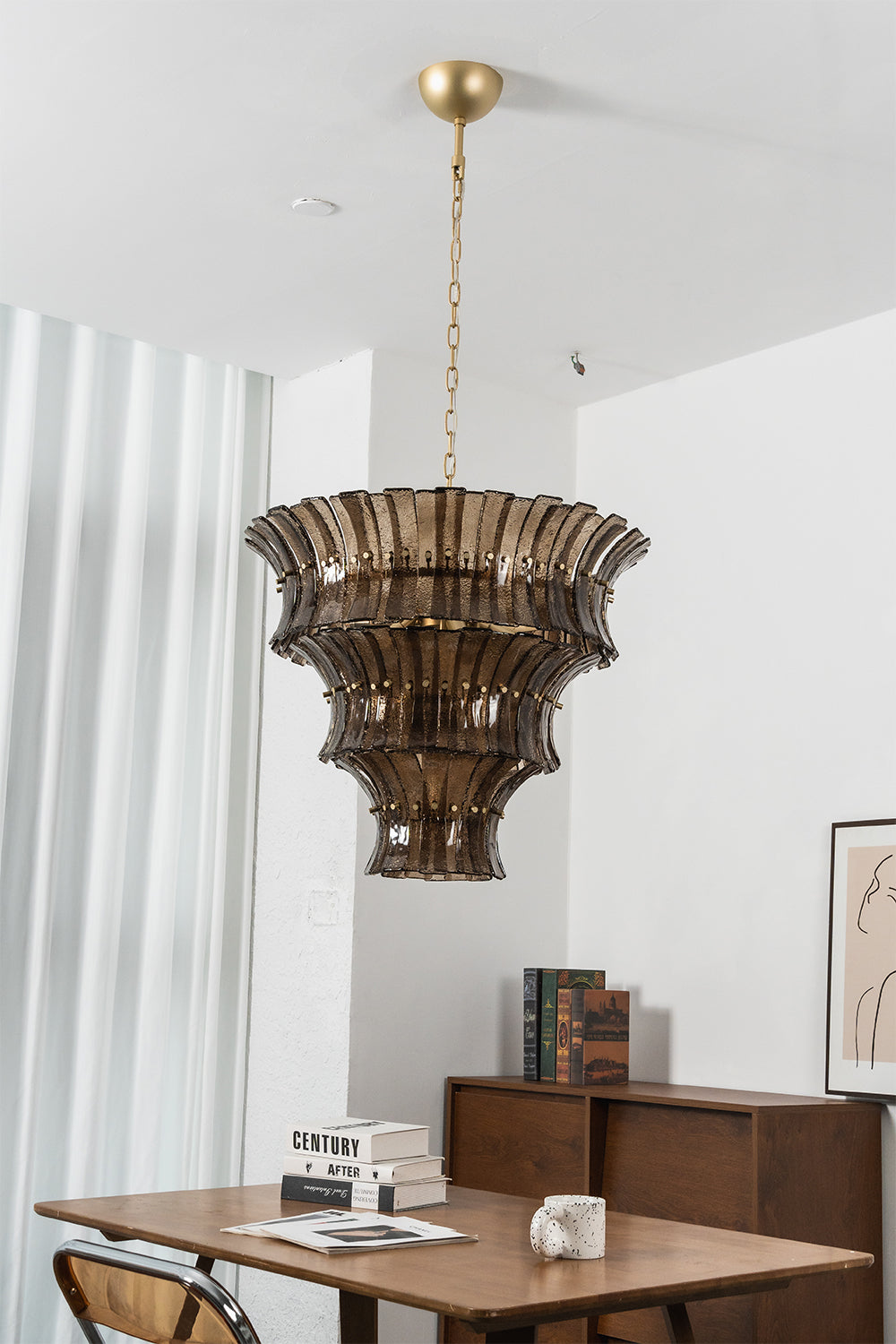 Octavia Sculptural Smoked Glass Chandelier | Dining Room Chandelier | Studio staged view of the fully illuminated tall multi-tiered glass fixture casting a warm golden glow near a table | Samu Lamp