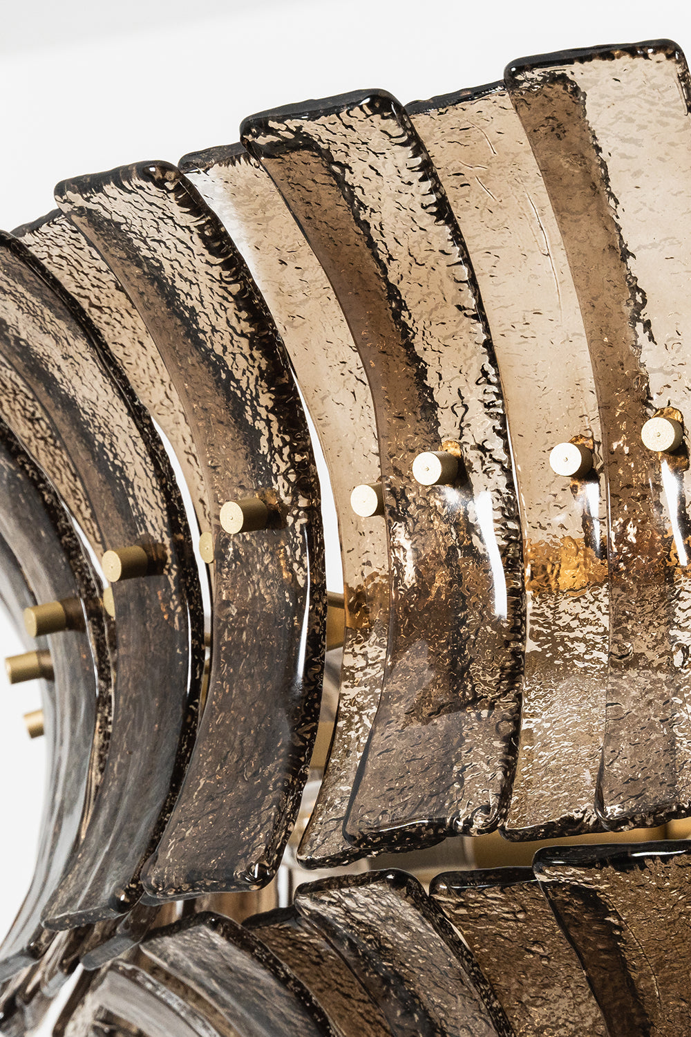 Octavia Sculptural Smoked Glass Chandelier | Overlapping Glass Detail | Close-up structural view focusing on the layered rows of curved smoked glass panels secured by gold metallic pins | Detail shot | Samu Lamp