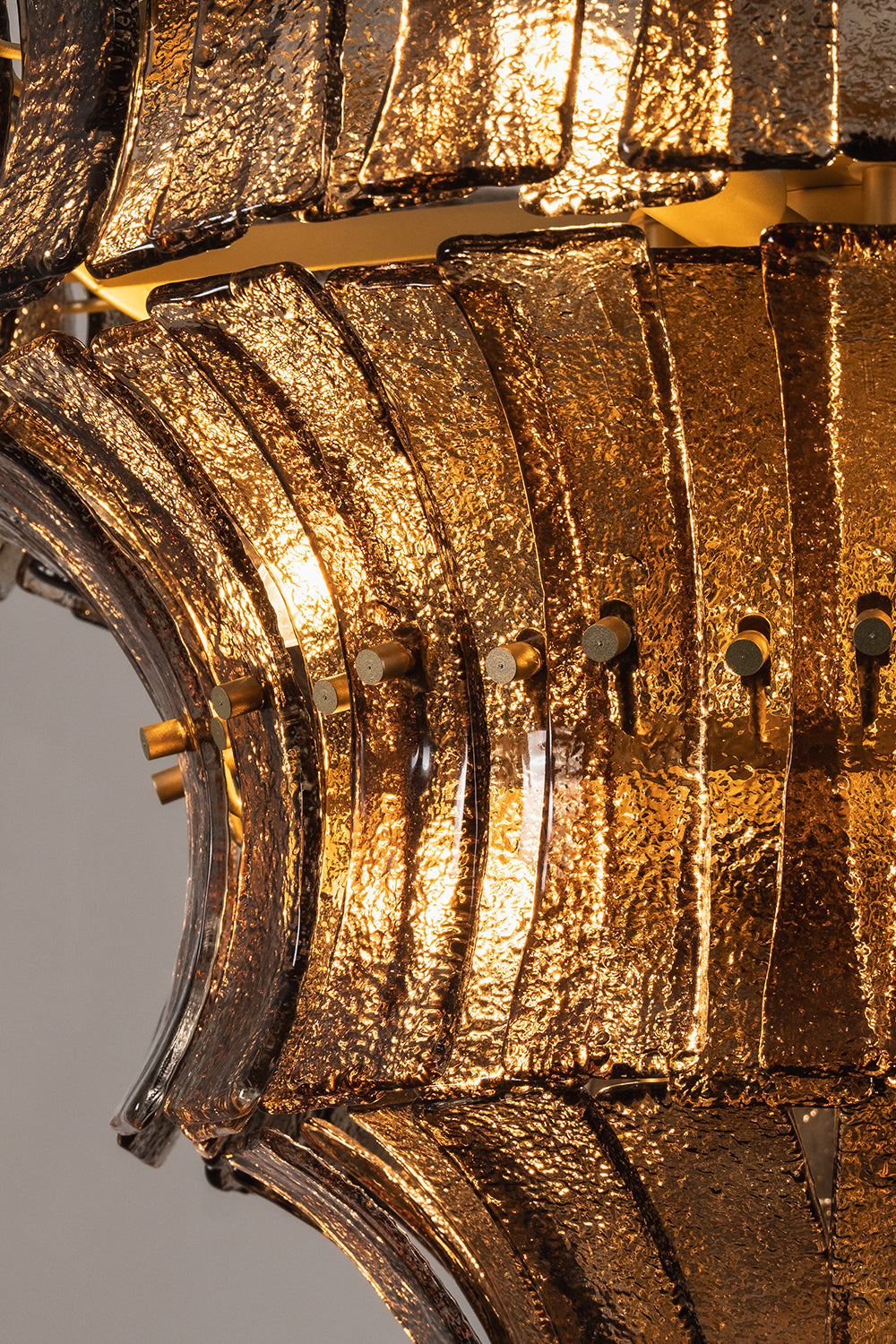 Octavia Sculptural Smoked Glass Chandelier | Illuminated Texture | Macro close-up view of the glowing glass panels highlighting the rich dimpled textures and warm amber gold light refraction | Detail shot | Samu Lamp