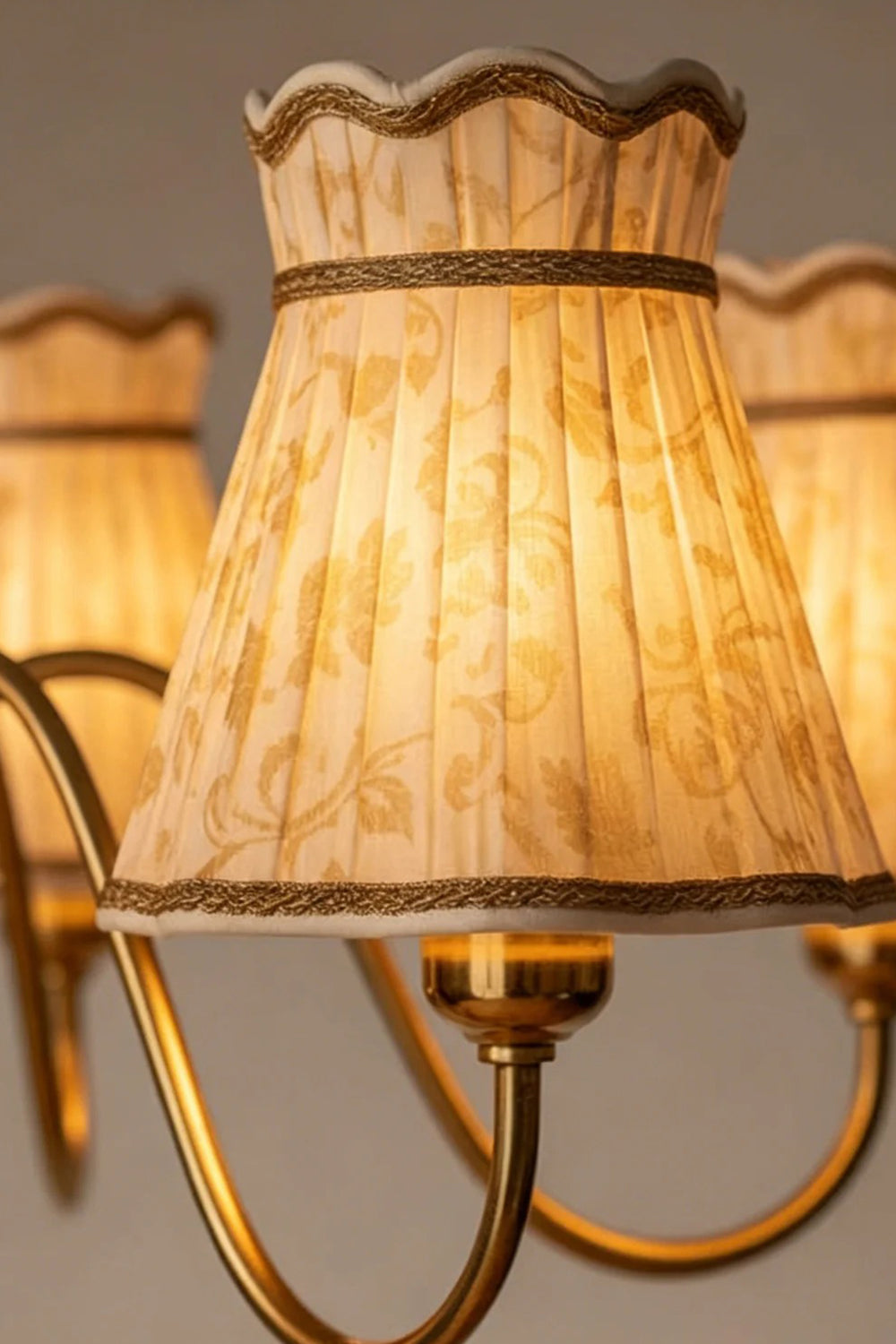 Odette Vintage Pleated Shaded Chandelier | Wood, Brass, Fabric | Macro close-up focus on a single fully illuminated cream fabric pleated shade highlighting its scalloped edge and fine braid trim | Detail shot | Samu Lamp