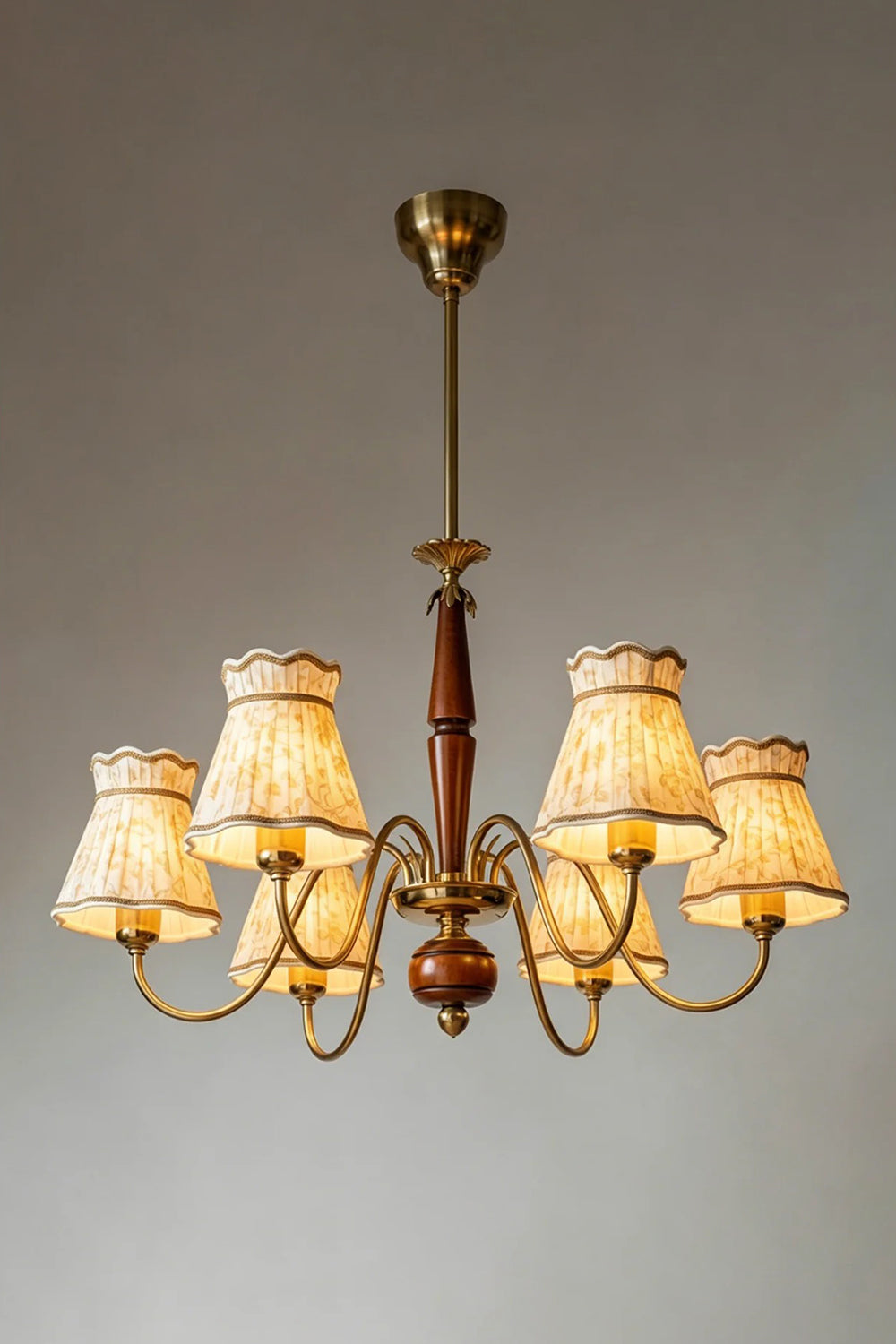 Odette Vintage Pleated Shaded Chandelier | Wood, Brass, Fabric | Studio view of the fully illuminated vintage chandelier casting a warm golden light halo through the pleated fabric shades against a grey background | Samu Lamp