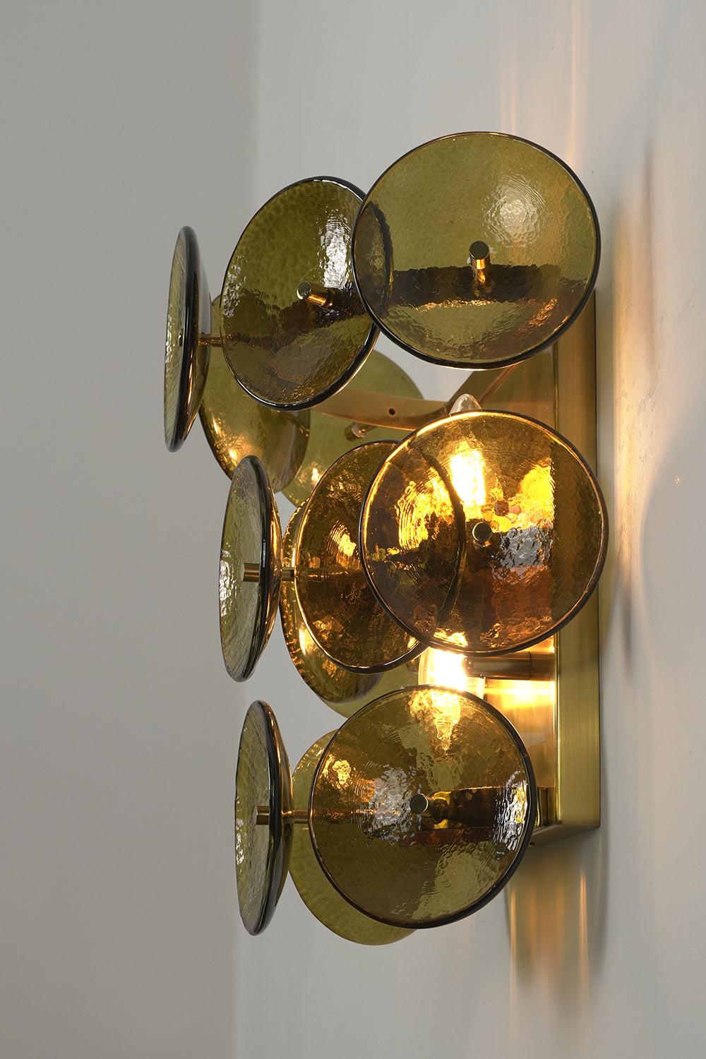 Lit tiered olive green hammered glass wall light | Metal, Glass | Angled lit product view showing tiered layers | Samu Lamp