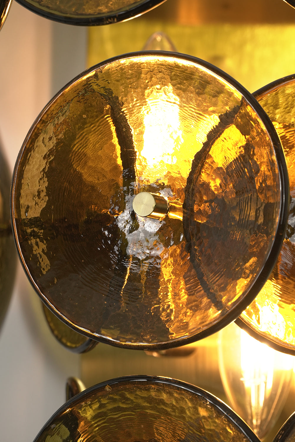 Close-up detail of lit hammered glass discs | Glass, Metal | Showing hammered texture and brass hardware connection | Samu Lamp