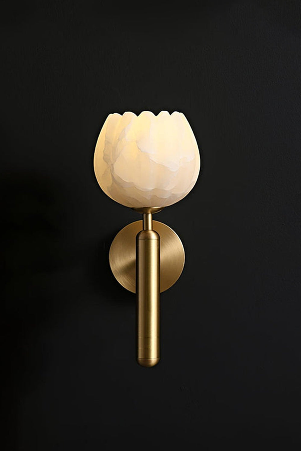 Ondine Alabaster Blossom Wall Sconce | Natural Alabaster and Brass | Minimalist perspective of the brass fixture glowing beautifully on a solid dark black background wall | Samu Lamp