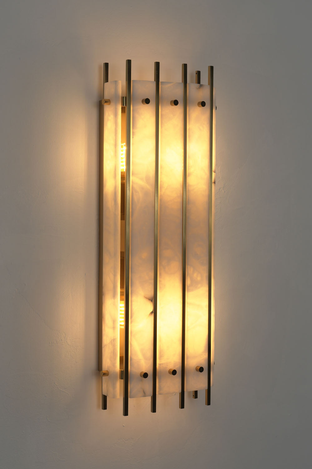 Ondrelle Bar Wall Sconce | Alabaster and Brass | Front illuminated view on dark wall with warm backlight | Samu Lamp