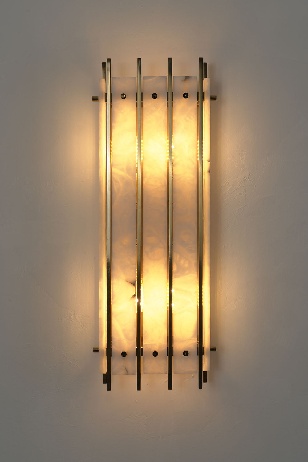 Ondrelle Bar Wall Sconce | Alabaster and Brass | Front illuminated view on dark wall with warm backlight | Samu Lamp