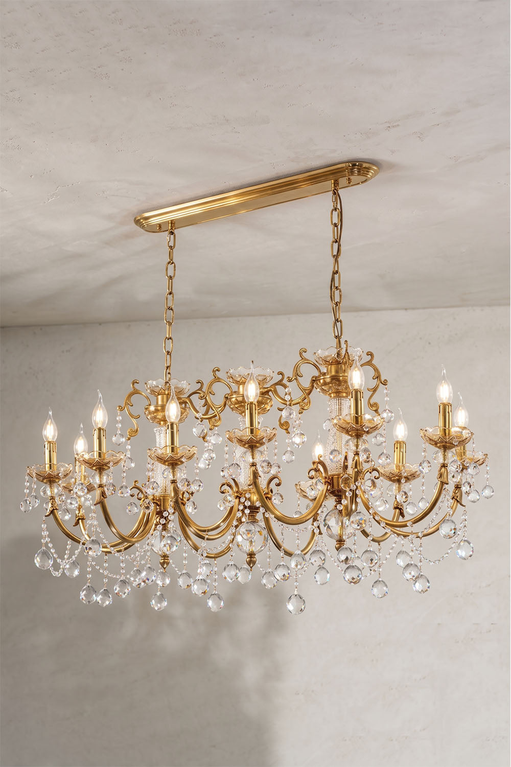 Orbessan Brass Crystal Oval Candle Chandelier | Cut Crystal and Brass | Full product view glowing brightly displayed against a plain grey wall | Samu Lamp