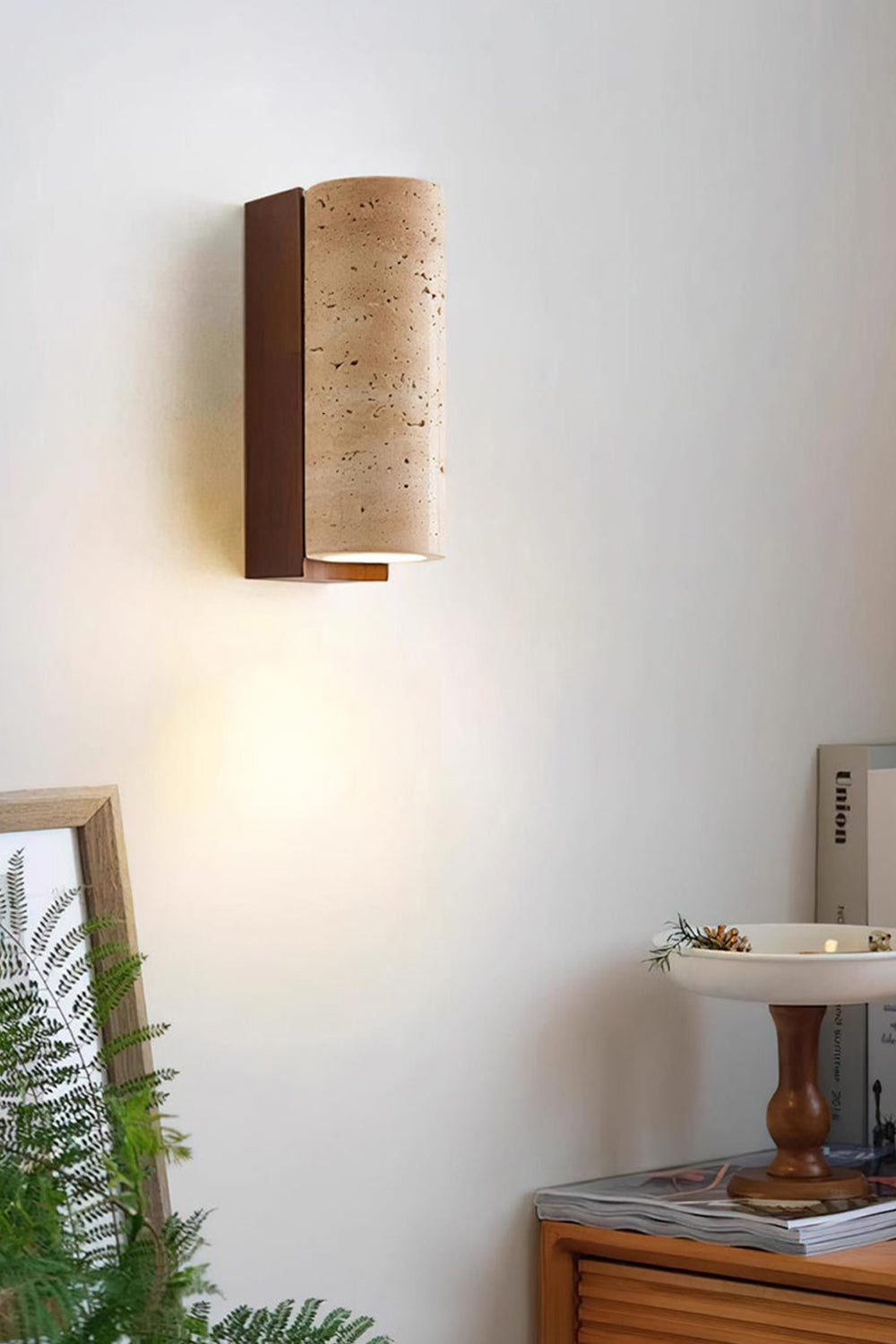 Outcrop Beige Travertine Wall Sconce | Travertine, Metal | Cozy indoor scene of the lit architectural stone sconce casting an organic glow near green house plants and a wooden shelf | Samu Lamp