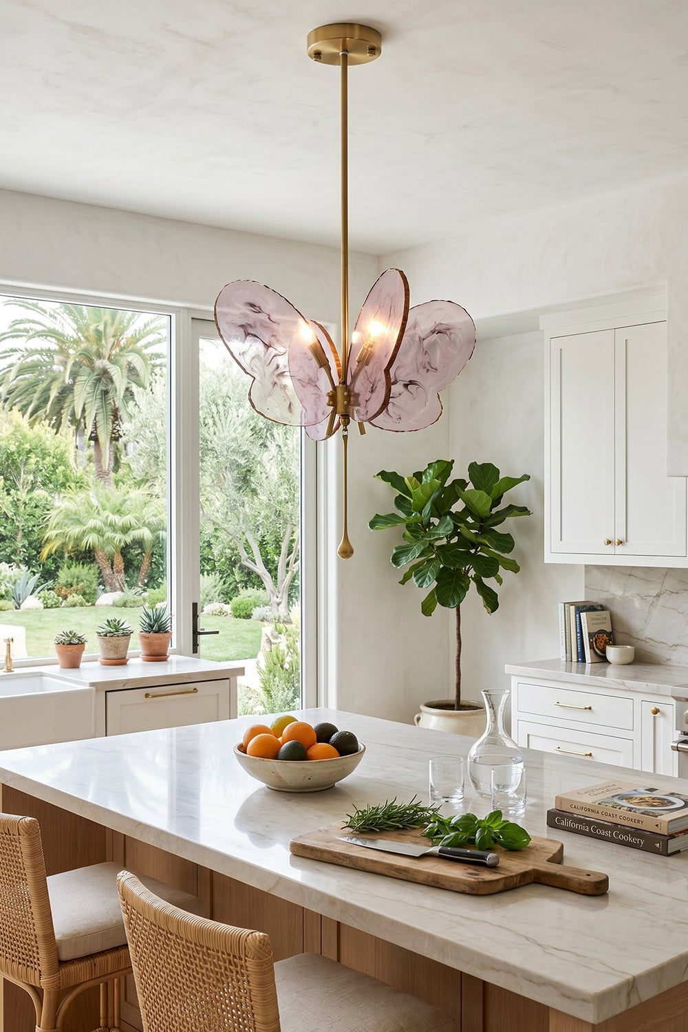 Papillon Glass Butterfly Pendant Lamp | Glass, Metal | Pink variant hanging over a white marble kitchen counter next to a large window showcasing garden views | Samu Lamp