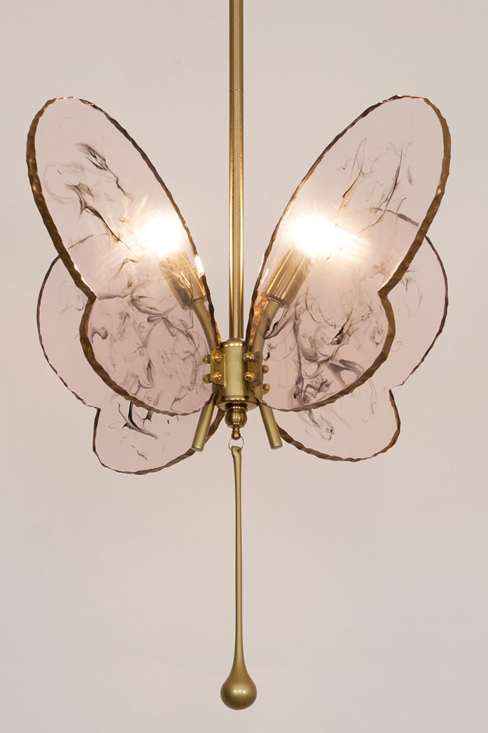 Papillon Glass Butterfly Pendant Lamp | Glass, Metal | Frontal straight-on view of the illuminated pink glass butterfly fixture throwing a warm backlight halo on a neutral wall | Samu Lamp