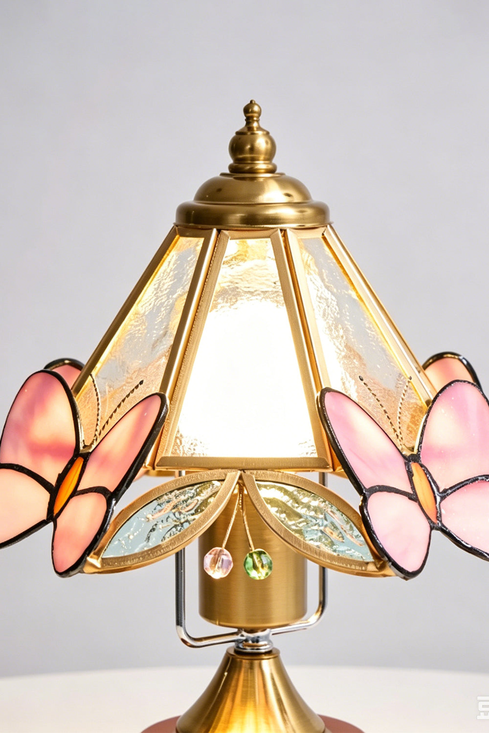 Papillon Heirloom Stained Table Lamp | Wood, Glass, Metal | Close-up frontal view of the lit stained glass shade highlighting the pink butterfly wings and brass frame | Detail shot | Samu Lamp