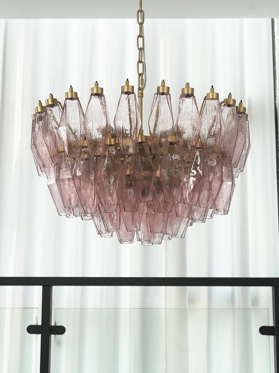 Lit pink glass polyhedron chandelier near a window | Metal, Glass | Close-up showing the warm glowing crystals | Samu Lamp