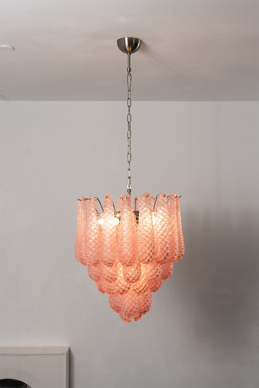 Amara Blush Cascading Glass Chandelier | Glass, Metal | Frontal view of the fully illuminated pink glass chandelier against a clean, plain studio wall | Samu Lamp
