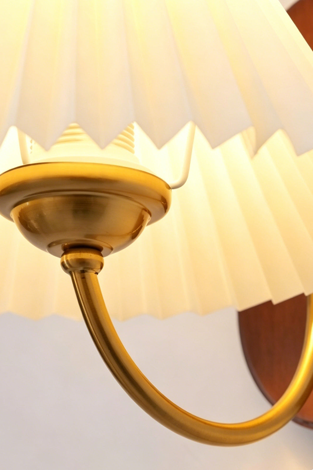 Pleated Fabric Wall Lamp | Fabric, Metal, Wood | Close-up view from underneath focusing on the curved brass support arm and light socket attachment | Detail shot | Samu Lamp