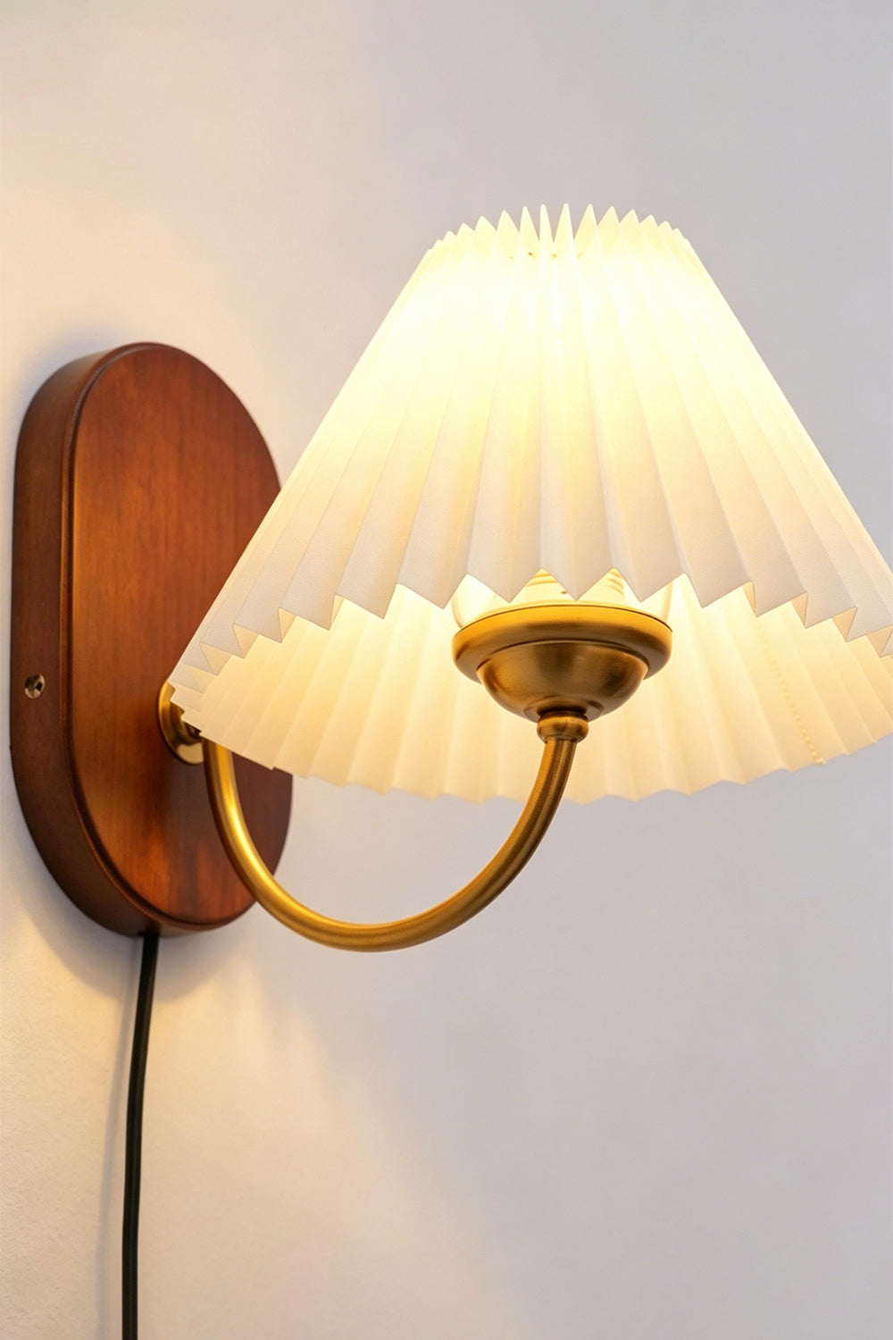 Pleated Fabric Wall Lamp | Fabric, Metal, Wood | Side angle profile view of the illuminated pleated lamp radiating soft ambient light on a plain wall with a visible black cord | Samu Lamp
